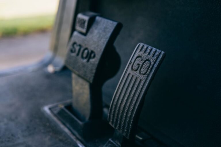 Close-up of a driver's right foot resting on the accelerator pedal in a car footwell, with the brake pedal beside it
