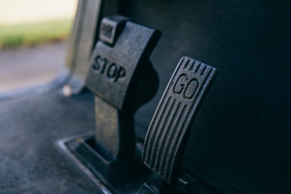 Close-up of a driver's right foot resting on the accelerator pedal in a car footwell, with the brake pedal beside it