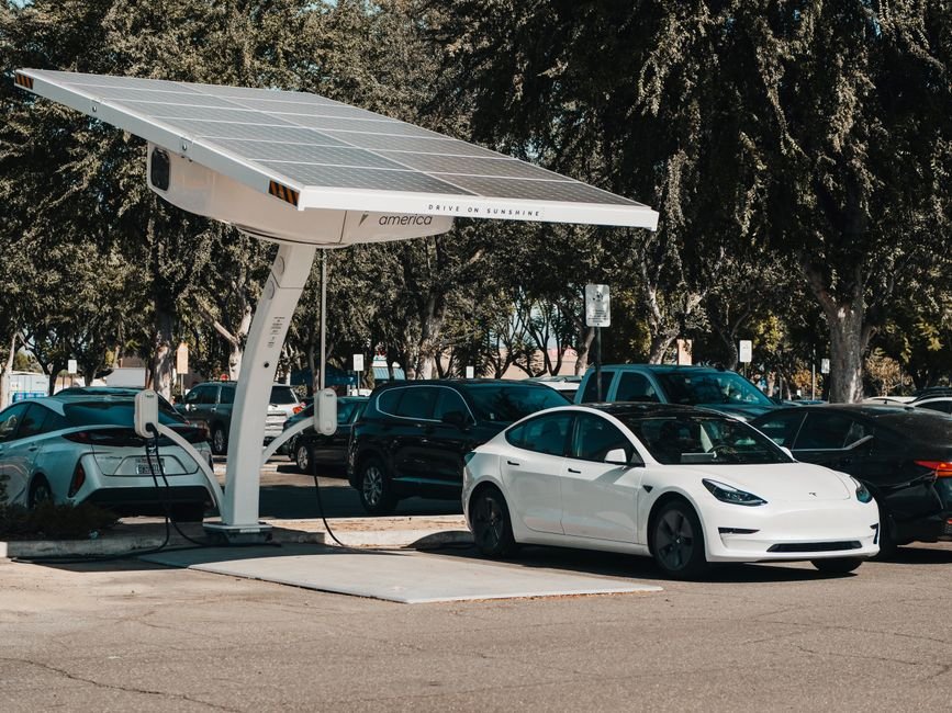 An electric car plugged into a home charger with rooftop solar panels visible above the garage