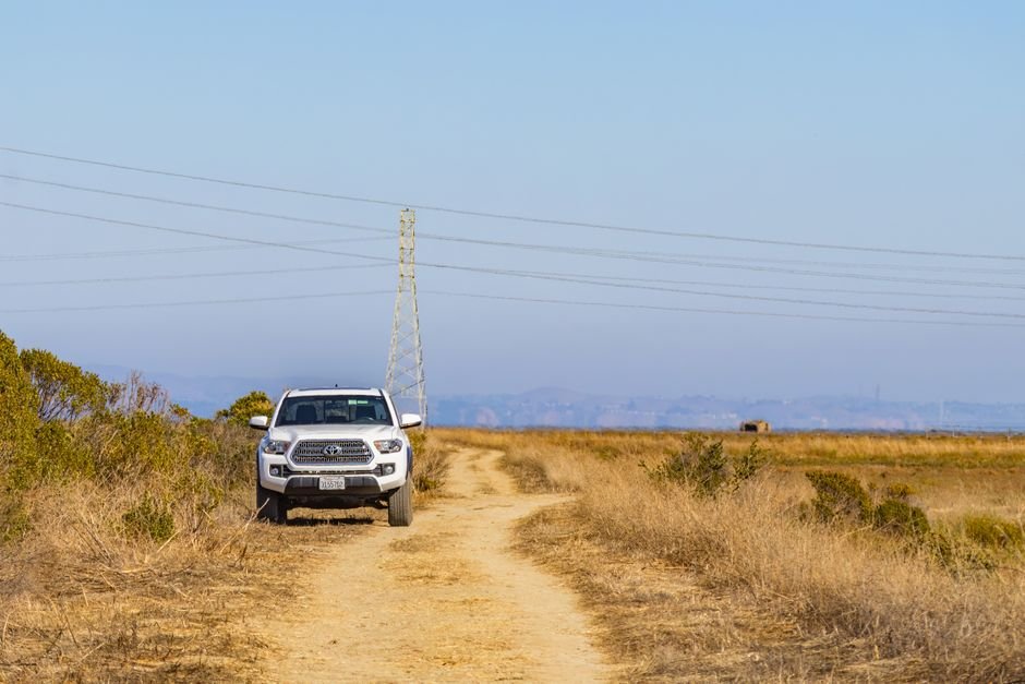 An electric car parked on the shoulder of an empty rural road with open fields around it