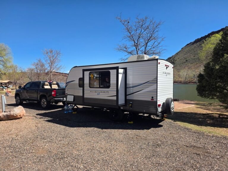 An electric pickup truck towing a small enclosed trailer along a paved road