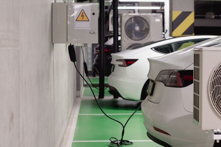 Row of wall-mounted EV chargers beside marked parking spaces in a concrete apartment parking garage