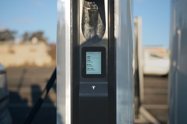 A hand holding a smartphone displaying a charging network app next to a public EV charging station