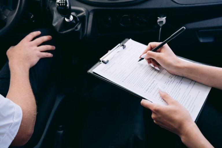 Printed insurance policy documents and a pen on a table, with an electric car parked outside the window