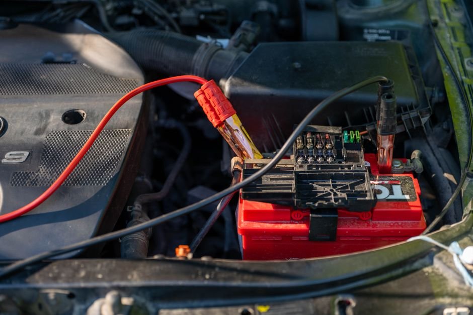 Red and black jumper cable clamps connected to a car battery terminal