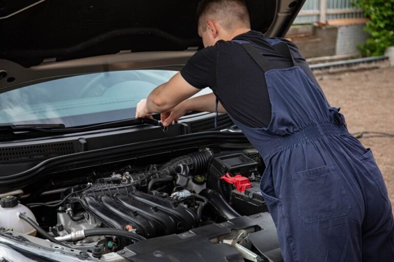 A mechanic leaning over an open hood listening to an engine running