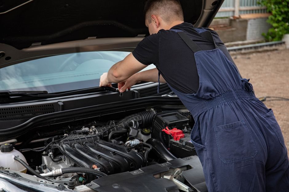 A mechanic leaning over an open hood listening to an engine running