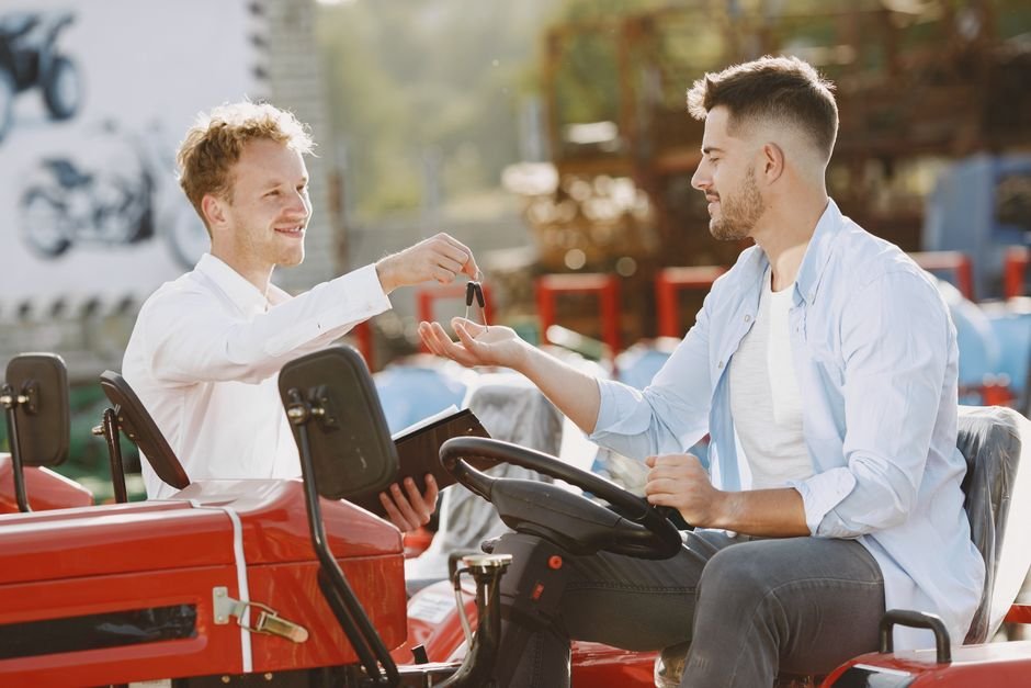 A seller handing car keys to a buyer over the hood of a parked car