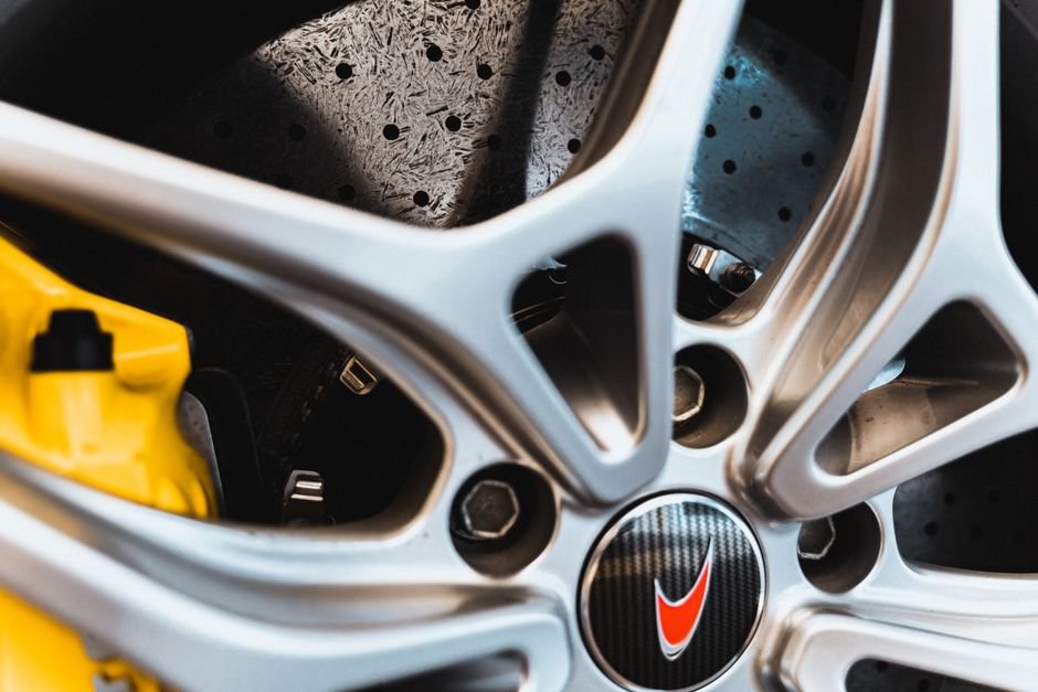 A person crouched beside a car wheel, looking through the spokes at the brake pad and rotor