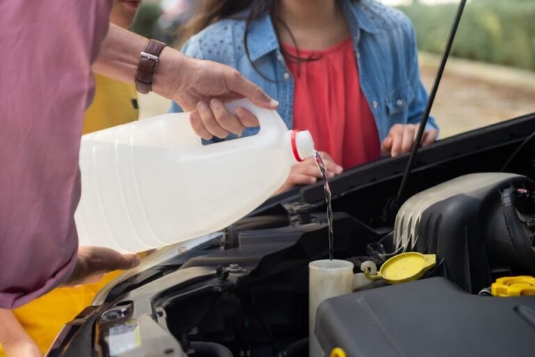 A bottle of winter windshield washer fluid being poured into a car's reservoir with frost visible on the hood